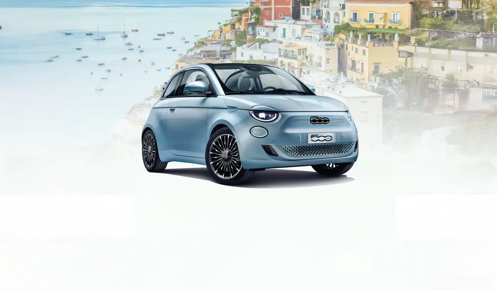 Fiat 500e con sfondo di città italiana costiera