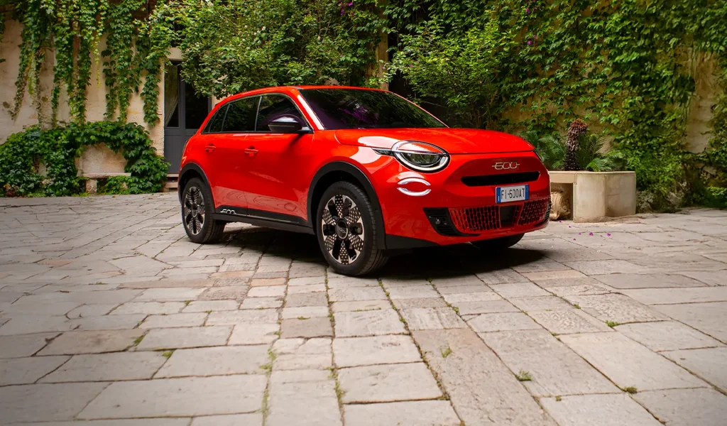 fiat 600e arancione con muro con edera come sfondo